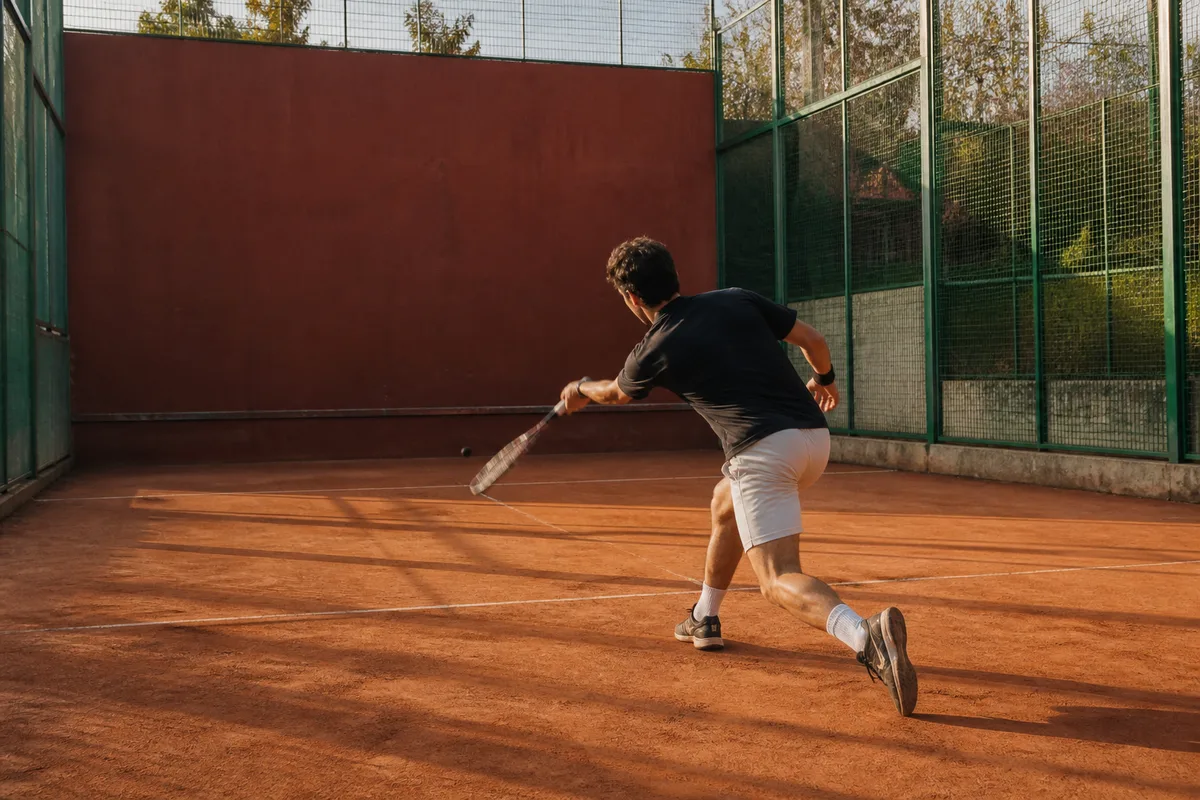 Joueur de squash frappant la balle contre le mur frontal dans un court ferme