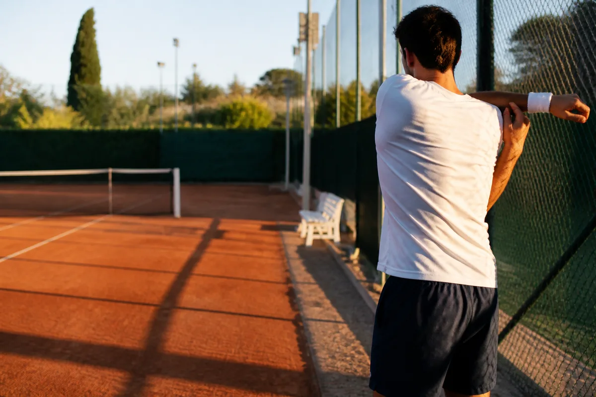 Joueur de tennis effectuant des rotations d epaules au bord du court avant un match